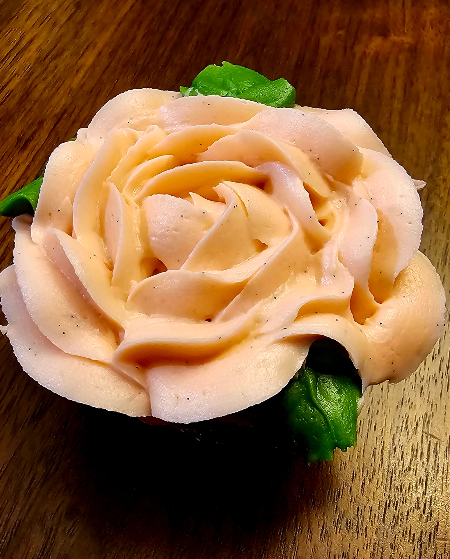 Single cupcake topped with a peach buttercream rose and green leaves