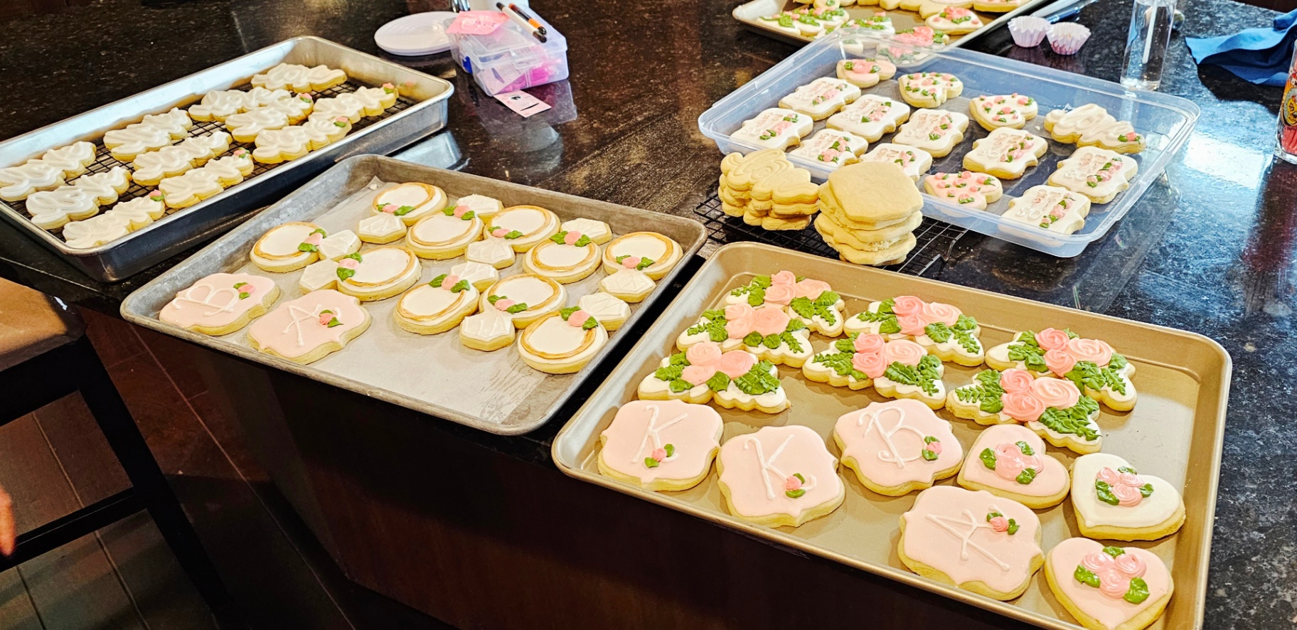 Trays of bridal shower monogram cookies with pink roses and greenery