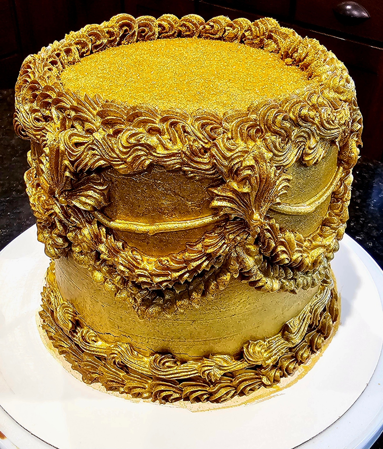 Tall ornate cake with intricate gold-painted buttercream piping