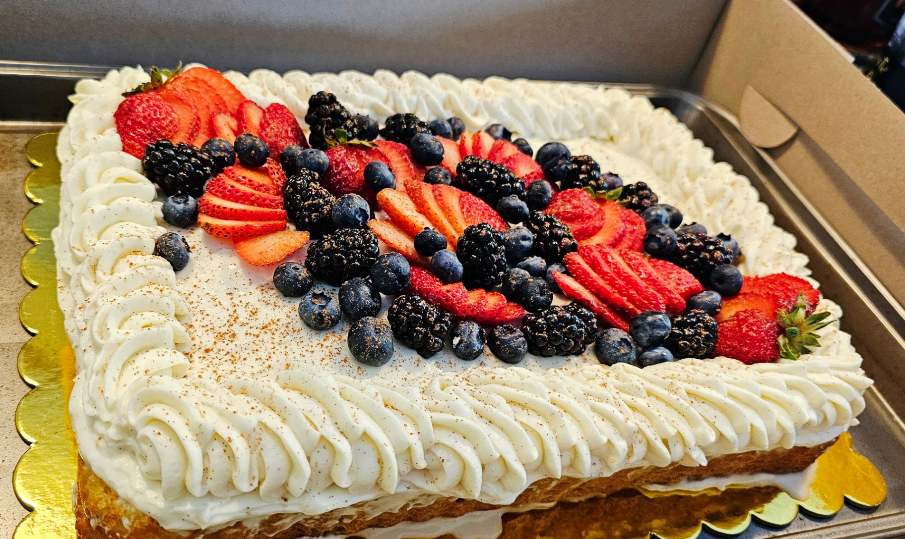 Tres leches cake topped with whipped cream, strawberries, blueberries, and blackberries