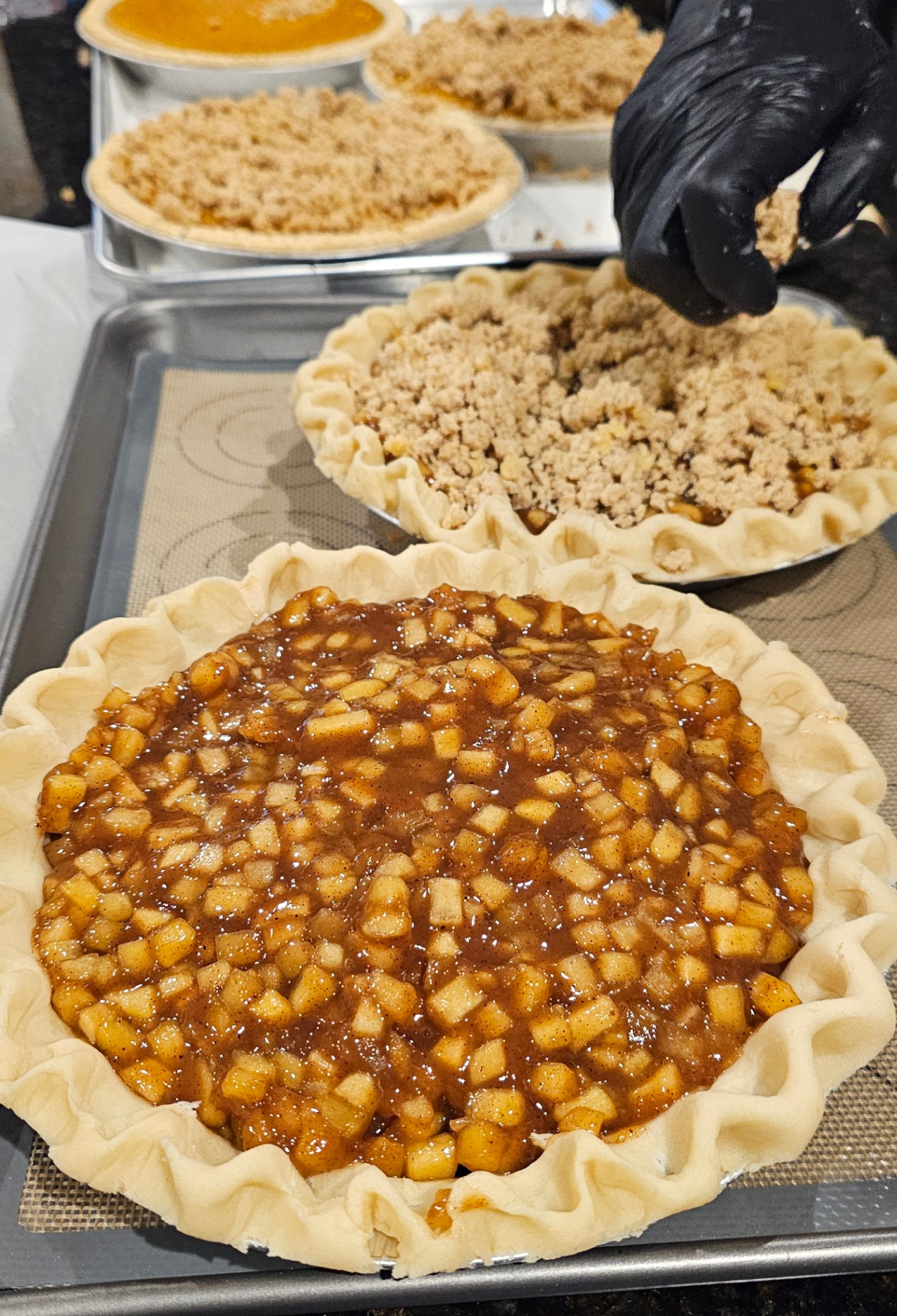 Fresh apple pie being assembled with cinnamon apple filling and streusel topping